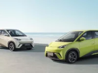 Dois BYD Dolphin Mini, um bege e um verde, estacionados em frente ao mar