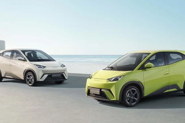 Dois BYD Dolphin Mini, um bege e um verde, estacionados em frente ao mar